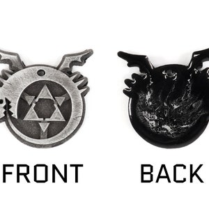 May include: A silver metal charm with a black and white design. The front of the charm features a circle with a triangle inside. The back of the charm is black with a white design.