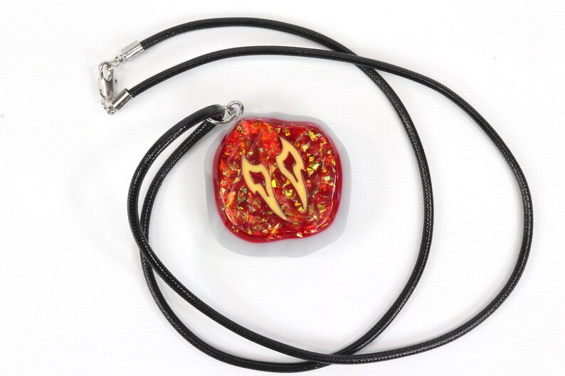May include: A red and gold pendant with a black cord necklace. The pendant is a square shape with a white border and a red and gold design inside.