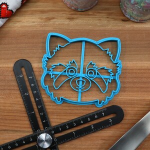 May include: Blue plastic cookie cutter shaped like a red panda face. The cutter has a detailed design with eyes, nose, and fur.