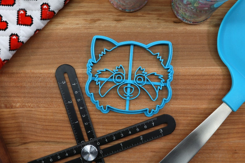 May include: Blue plastic cookie cutter shaped like a red panda face. The cutter has a detailed design with eyes, nose, and fur.