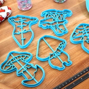 May include: A set of five blue plastic mushroom-shaped cookie cutters on a wooden surface.
