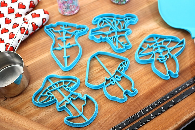 May include: A set of five blue plastic mushroom-shaped cookie cutters on a wooden surface.