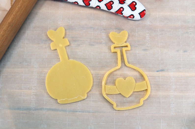 May include: Two yellow cookie cutters shaped like bottles with heart-shaped tops. The bottle on the right has a heart-shaped design on the front.