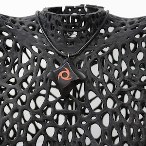 May include: A black necklace with a star-shaped pendant featuring a red and orange swirl design. The necklace is displayed on a black, 3D printed, lattice-like mannequin.