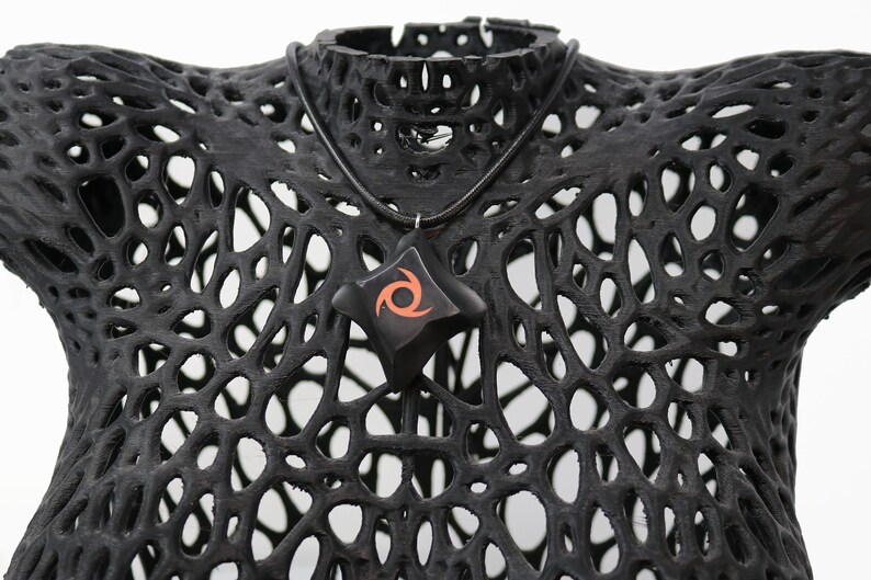 May include: A black necklace with a star-shaped pendant featuring a red and orange swirl design. The necklace is displayed on a black, 3D printed, lattice-like mannequin.