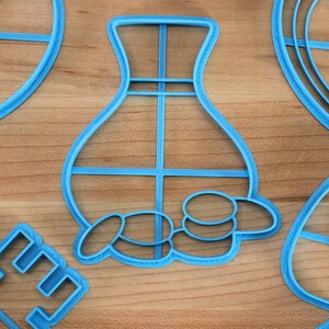 May include: A set of five blue plastic cookie cutters in various shapes, including a vase, a key, a heart, and two leaves. The cutters are on a wooden surface.