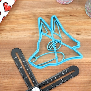 May include: A blue plastic cookie cutter shaped like a dog's head. The cutter is on a wooden surface.