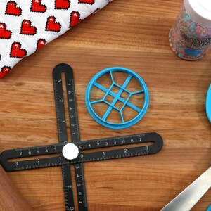 May include: A black ruler with a rotating dial and a blue plastic circle cutter. The cutter has a grid pattern and is used for making cookies or other pastries.