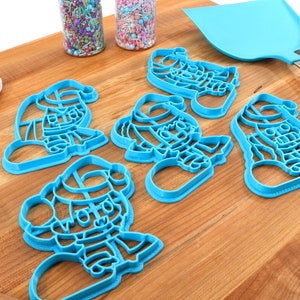 May include: Set of five blue plastic cookie cutters shaped like Santa Claus. The cutters are on a wooden cutting board.