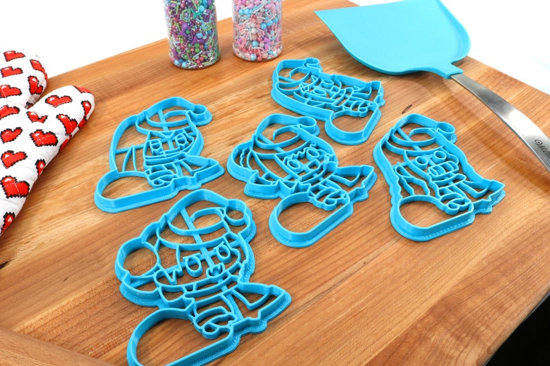 May include: Set of five blue plastic cookie cutters shaped like Santa Claus. The cutters are on a wooden cutting board.