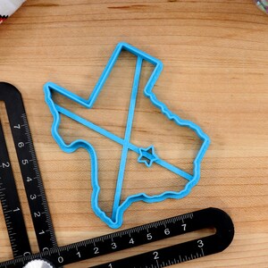 May include: A blue plastic cookie cutter shaped like the state of Texas with a star in the center.