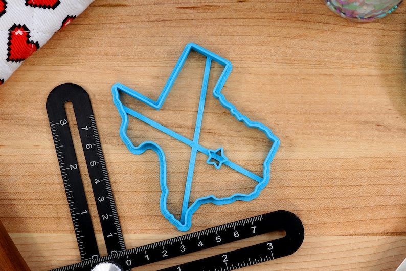 May include: A blue plastic cookie cutter shaped like the state of Texas with a star in the center.