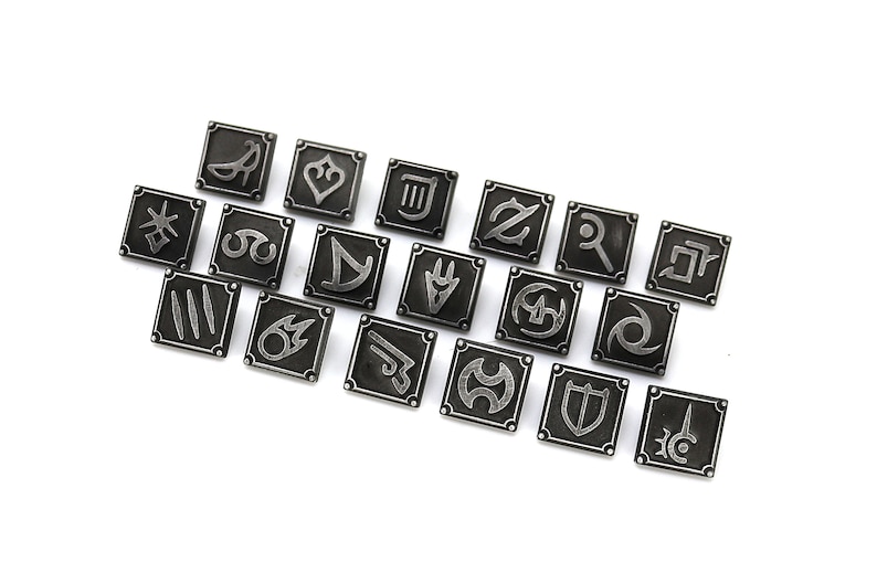 Puede incluir: Un conjunto de 18 pines de metal plateados con varios s&iacute;mbolos, incluyendo una espada, un escudo, una corona y un coraz&oacute;n. Los pines est&aacute;n dispuestos en un semic&iacute;rculo sobre un fondo blanco.