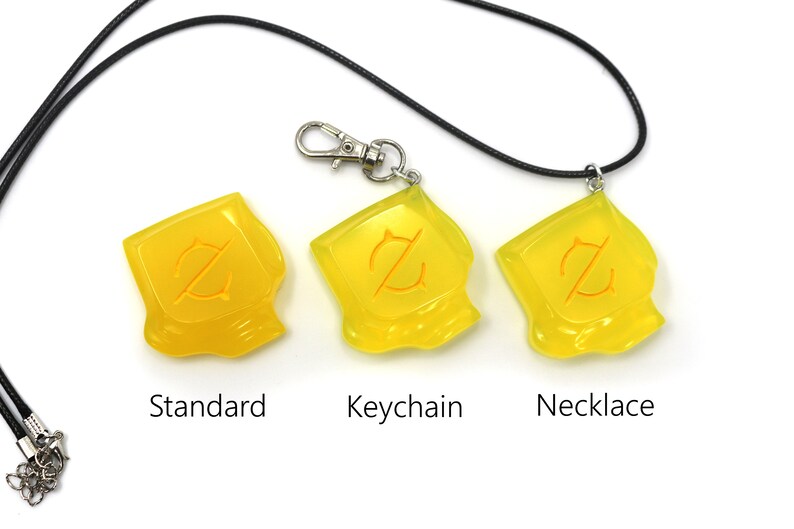 May include: Three yellow pendants with an orange design, labeled "Standard", "Keychain", and "Necklace". The "Keychain" version has a silver clasp. The "Necklace" version is on a black cord. All are on a white background.