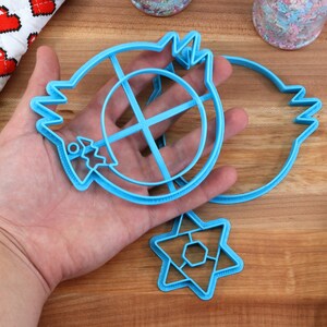 May include: Three blue plastic cookie cutters: a round cutter with a cross inside, a crescent moon shape, and a six-pointed star.