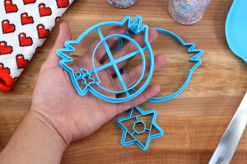 May include: Three blue plastic cookie cutters: a round cutter with a cross inside, a crescent moon shape, and a six-pointed star.