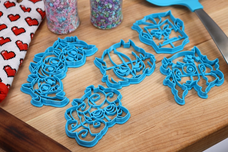 May include: Five blue plastic cookie cutters shaped like cartoon characters. The cutters are on a wooden surface.
