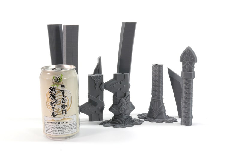 May include: A set of seven grey 3D printed sword parts, including a hilt, blade, and pommel. The parts are arranged on a white surface next to a can of Japanese beer.