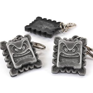 May include: Three silver-colored keychains featuring a pixelated angry face. The keychains are attached to silver rings.