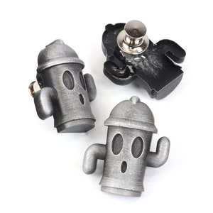 Może przedstawiać: Trzy srebrne metalowe szpilki w kształcie hydrantu przeciwpożarowego z kreskówkowymi twarzami. Szpilki mają zapięcie na szpilkę bezpieczeństwa z tyłu.