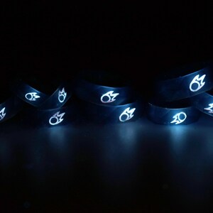 May include: A group of eight black silicone rings with a white flame design. The rings are stacked on top of each other and are glowing in the dark.