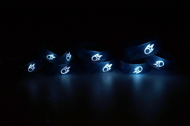 May include: A group of eight black silicone rings with a white flame design. The rings are stacked on top of each other and are glowing in the dark.