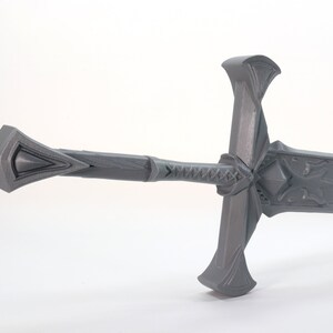 May include: A gray, detailed, 3D printed sword with a decorative hilt and a blade with intricate carvings.