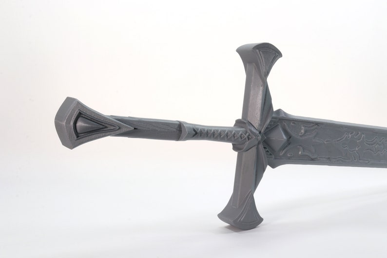 May include: A gray, detailed, 3D printed sword with a decorative hilt and a blade with intricate carvings.
