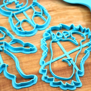 May include: A set of four blue plastic cookie cutters shaped like a bear, a footprint, a snowman, and a person. The cutters are on a wooden surface.