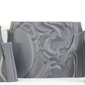 May include: Three gray 3D printed pieces with intricate, swirling designs. The pieces are made of a smooth, plastic-like material and have a slightly textured surface.