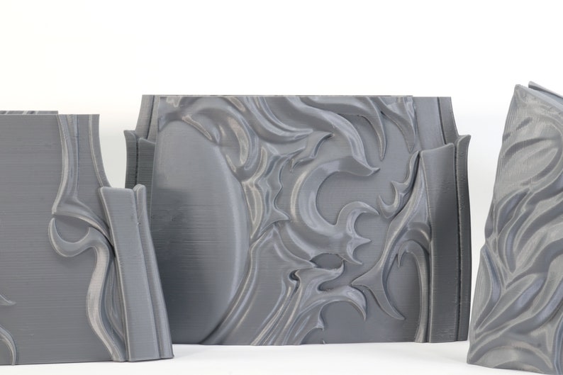 May include: Three gray 3D printed pieces with intricate, swirling designs. The pieces are made of a smooth, plastic-like material and have a slightly textured surface.