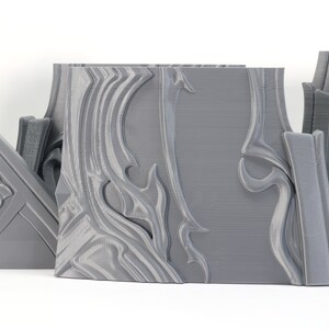 May include: Three gray 3D printed pieces with intricate, swirling designs. The pieces are made of a smooth, plastic-like material and have a slightly textured surface.