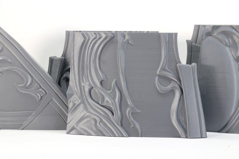 May include: Three gray 3D printed pieces with intricate, swirling designs. The pieces are made of a smooth, plastic-like material and have a slightly textured surface.