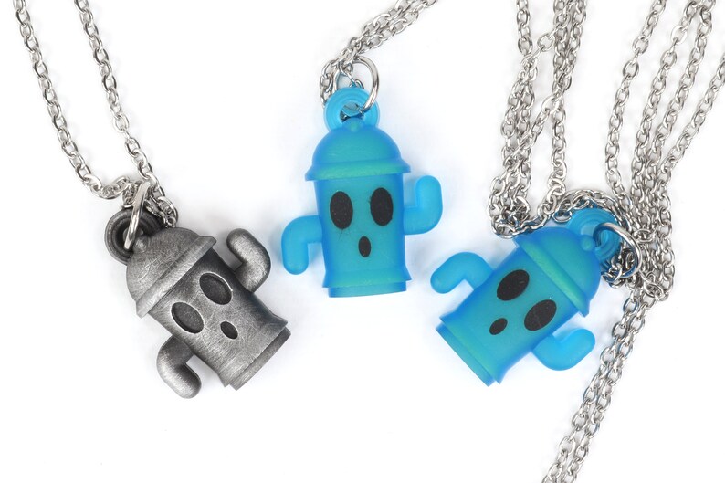 May include: Three silver chain necklaces with a blue and silver cactus pendant. The cactus pendant has a cartoon face with two eyes and a mouth.