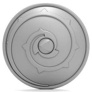 Puede incluir: Un escudo circular gris con un dise&ntilde;o de espiral estilizado en el centro. El escudo tiene un borde elevado y una superficie texturizada.