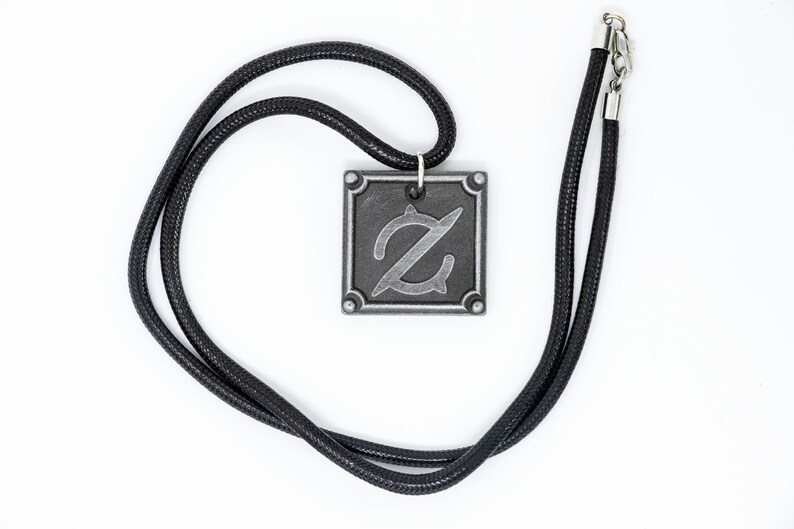 Pu&ograve; includere: Una collana con cordoncino nero con un ciondolo quadrato argentato con una lettera Z stilizzata.