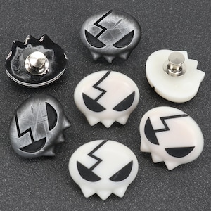 Peut inclure: Six boutons en forme de cr&acirc;ne avec un motif craquel&eacute;. Trois boutons sont noirs avec des d&eacute;tails blancs et trois boutons sont blancs avec des d&eacute;tails noirs. Chaque bouton a un embout m&eacute;tallique au dos.