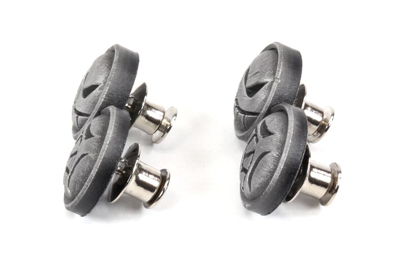 Op de afbeelding: Twee sets zwarte metalen drukknopen met een decoratief ontwerp. Elke knop heeft een ronde, platte bovenkant met een reli&euml;f en een zilveren metalen pen.