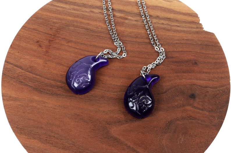 May include: Two silver chains with purple glass pendants shaped like a crescent moon. The pendants have intricate designs carved into them.