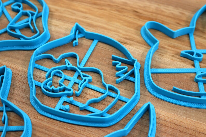 May include: A set of four blue plastic cookie cutters shaped like different animals. The cutters are on a wooden surface.