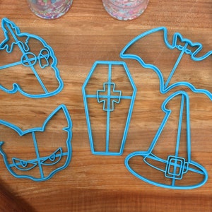 May include: Set of five blue plastic Halloween cookie cutters. The cutters are shaped like a ghost, a bat, a coffin, a witch's hat, and a cat.