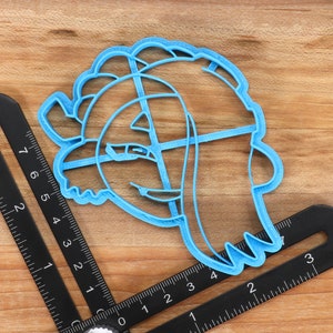 May include: A light blue plastic cookie cutter shaped like a cartoon character with a large head and a small body. The cutter is about 3 inches tall and 2 inches wide.