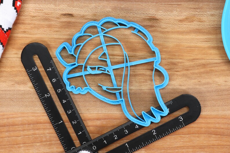 May include: A light blue plastic cookie cutter shaped like a cartoon character with a large head and a small body. The cutter is about 3 inches tall and 2 inches wide.