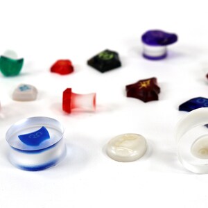 May include: A collection of colorful dice and tokens for a board game. The dice are made of clear plastic with different colored accents. The tokens are made of various materials, including plastic, metal, and wood.