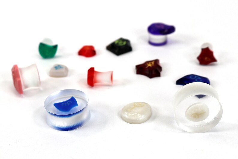May include: A collection of colorful dice and tokens for a board game. The dice are made of clear plastic with different colored accents. The tokens are made of various materials, including plastic, metal, and wood.