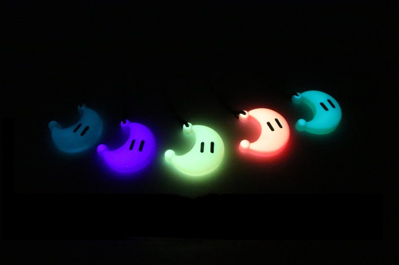 May include: Five glow-in-the-dark crescent moon charms in different colors: teal, purple, green, pink, and blue. Each charm has two small black dots for eyes.
