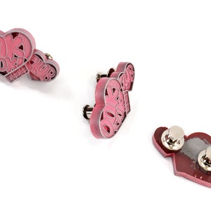 May include: Three pink heart-shaped pins with the text "DOK DOK CLUB" on them. The pins have silver metal backs with a pin and a safety clasp.