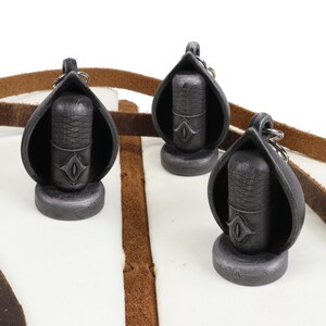 May include: Three silver and black microphone-shaped keychains with a leather strap. Each keychain has a small eye design on the front.