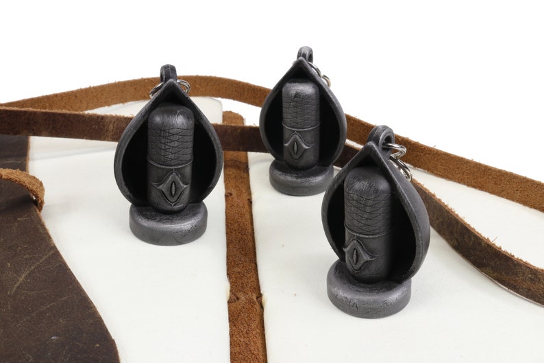 May include: Three silver and black microphone-shaped keychains with a leather strap. Each keychain has a small eye design on the front.
