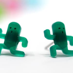 May include: A pair of green plastic earrings shaped like running figures. Each figure has a simple face with two eyes and a mouth.